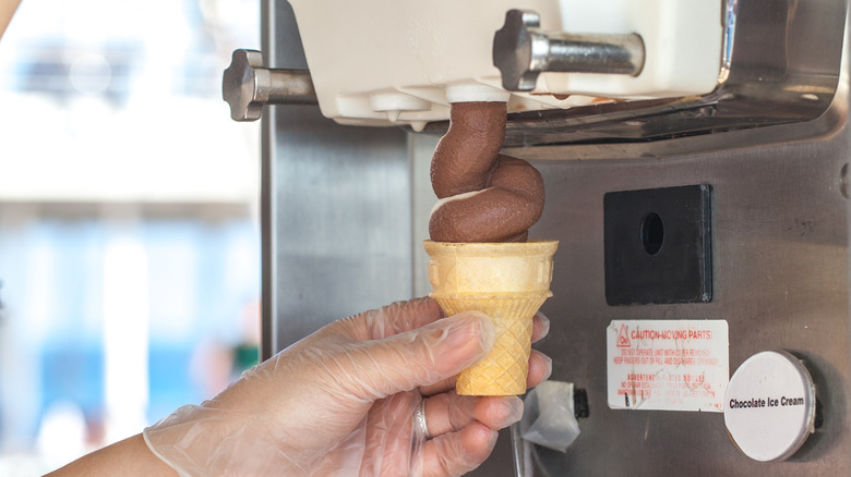 Person filling chocolate-vanilla soft serve cone