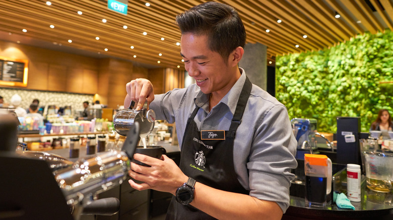 Happy Starbucks barista pouring hot coffee 