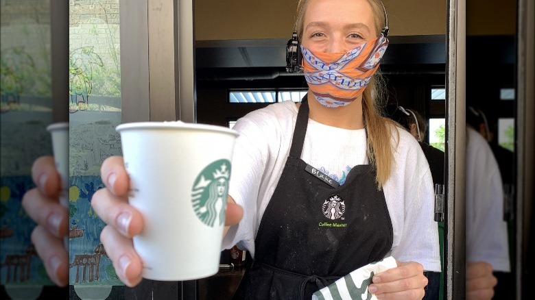 A masked Starbucks employee handing a drink through the drive-thru