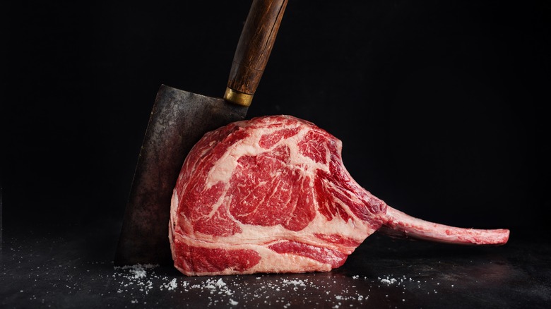 raw tomahawk steak next to cleaver