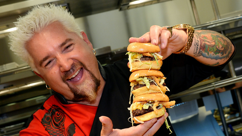 Guy Fieri holding a triple-stacked burger