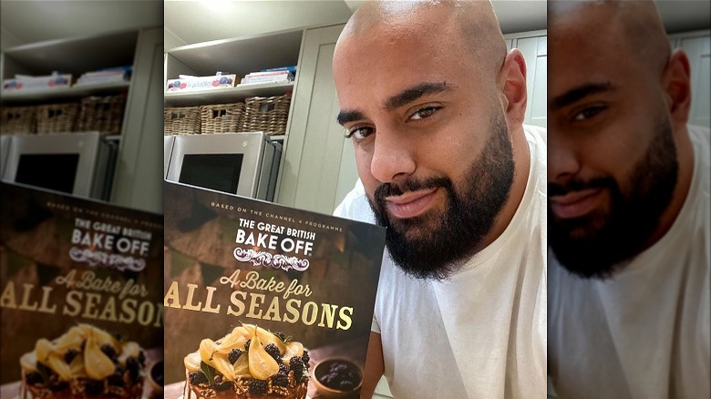 George holding with GBBO book in home kitchen