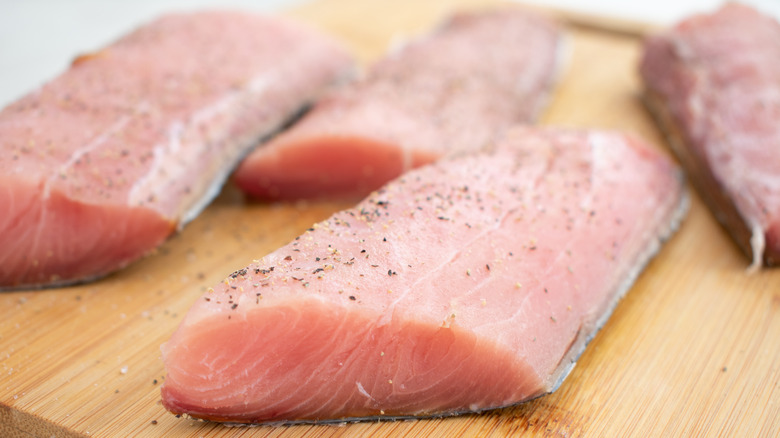 Raw mahi mahi fillets on a cutting board seasoned with pepper