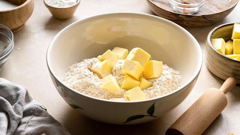 Cubed butter in bowl of flour next to rolling pin 