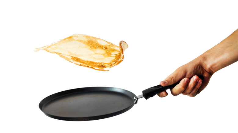 A man holding a frying pan, flipping pancakes