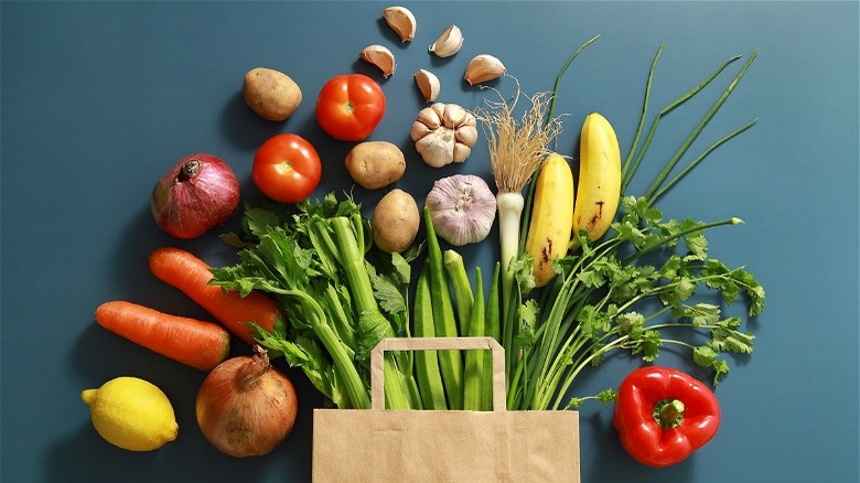 Vegetables pouring out of brown bag, blue background 