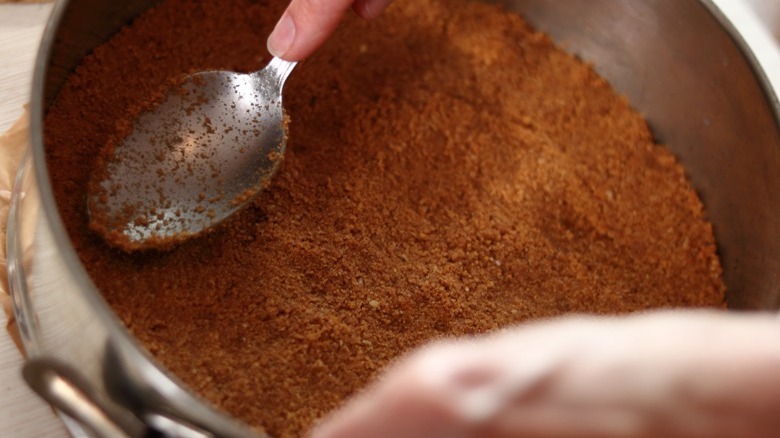 Hands using a spoon to press crust into a springform pan