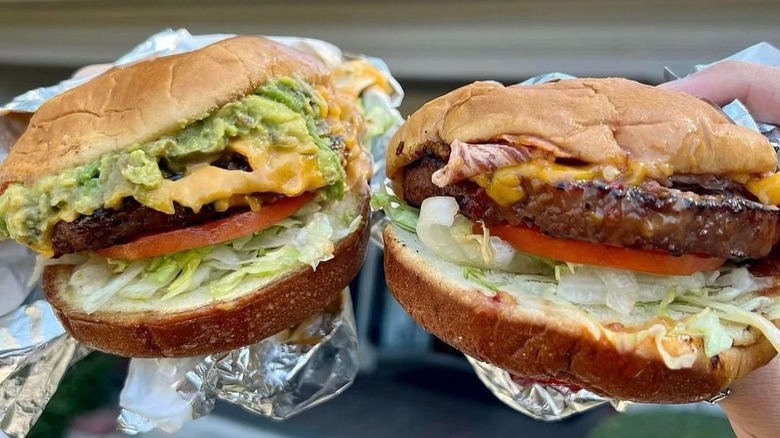 holding up two plant-based burgers