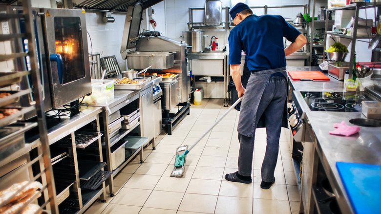 Kitchen porter mopping the floor in a commercial kitchen