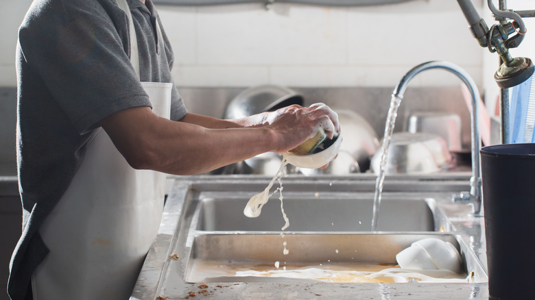 Dishwasher in restaurant kitchen washing a bowl