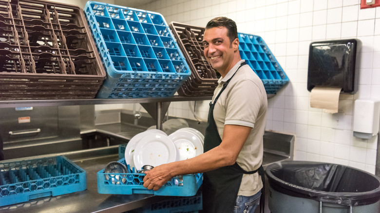 Dishwasher smiling and carrying tray of dirty plates