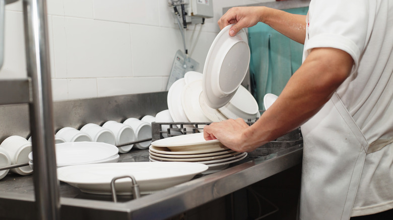 Dishwasher stacking dried plates in restaurant kitchen