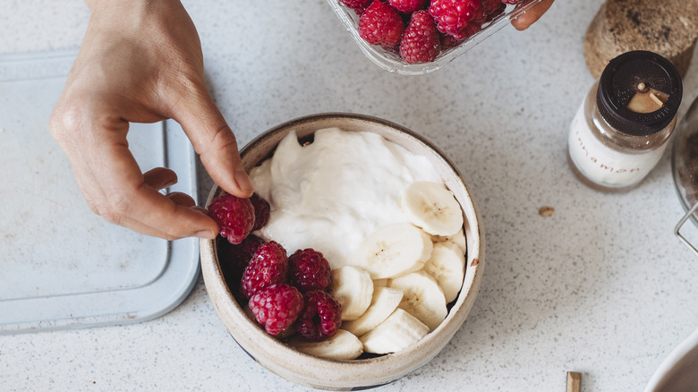 person topping yogurt with fruit