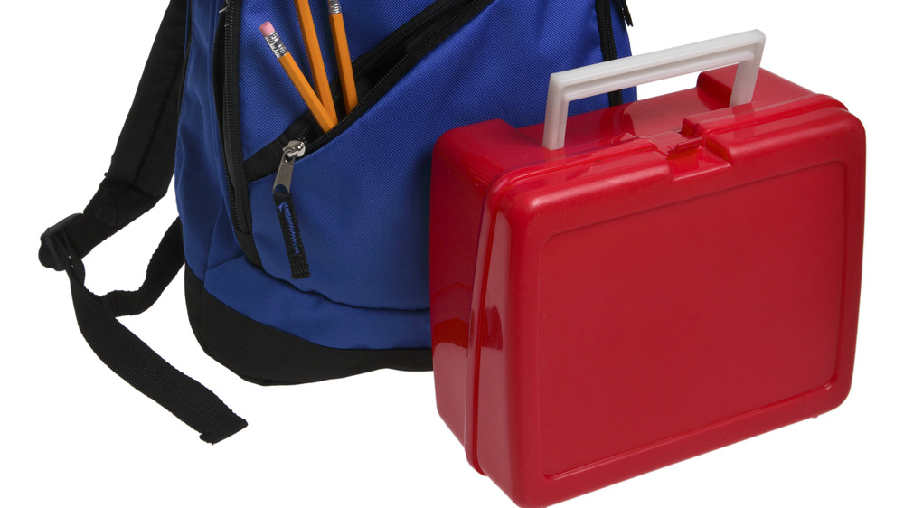 Plastic red lunch box in front of a blue backpack