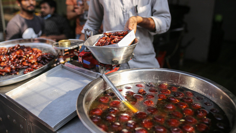 Person making gulab juman with large metal pots