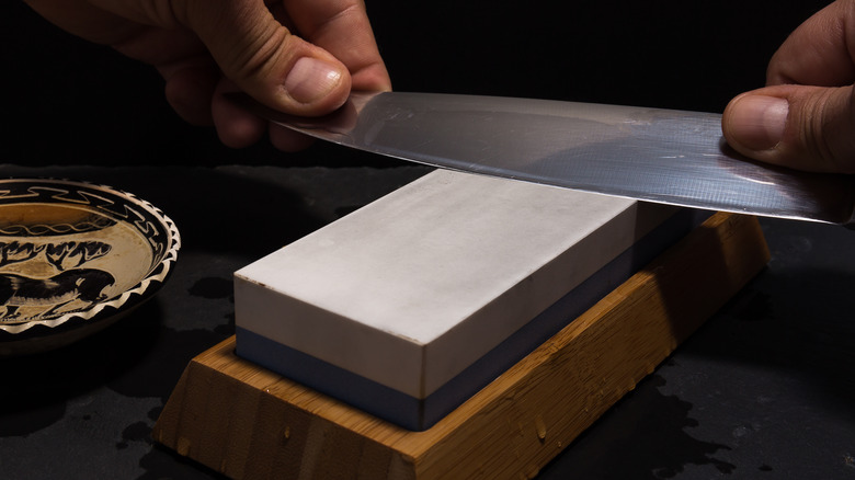 Hands sharpen knife on whetstone