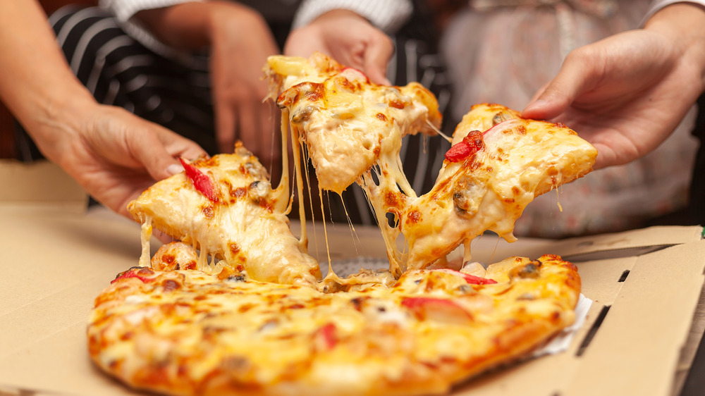 Three hands grabbing pizza slices with cheese pulls from pie