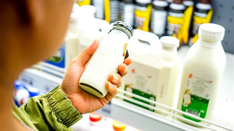 Person holding glass bottle of milk in refrigerated section of store