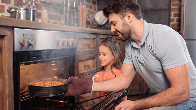 Father and daughter removing cake from oven