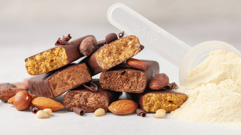 A pile of protein bars and nuts next to a scoop of protein powder