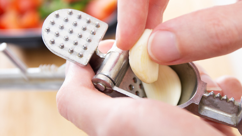 hands putting two cloves of garlic into a garlic press