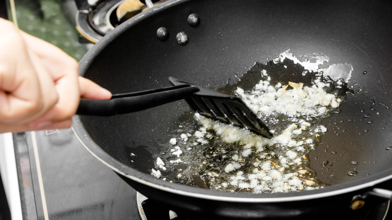 minched garlic being sauteed in oil in a nonstick pan and stirred with a spatula