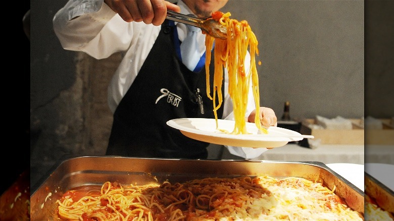 Server making a plate of spaghetti from a large hotel pan of spagetti