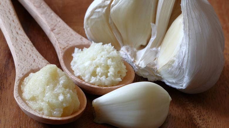 spoonfulls of minced garlic and garlic puree next to a head and cloves of fresh garlic