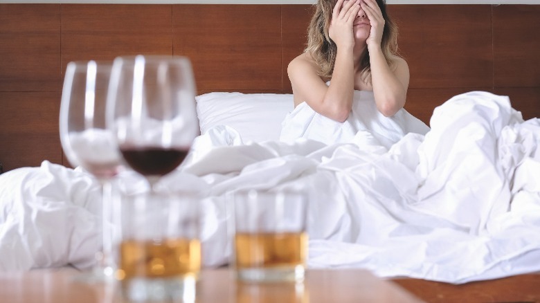 wine and liquor glasses in front of woman in bed with hangover