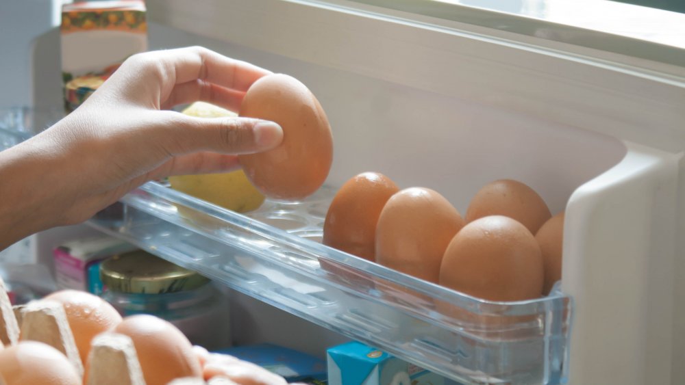 Close up of woman's hands placing eggs from a carton into the egg container of a refrigerator door.