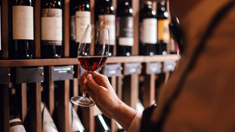 Hand holding glass of wine in front of bottles