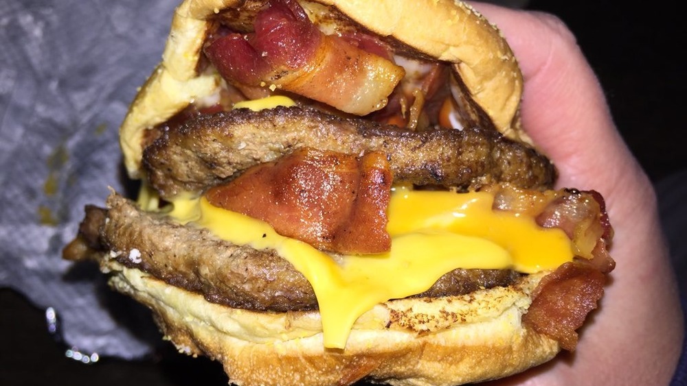 Man holding burger with bacon and cheese