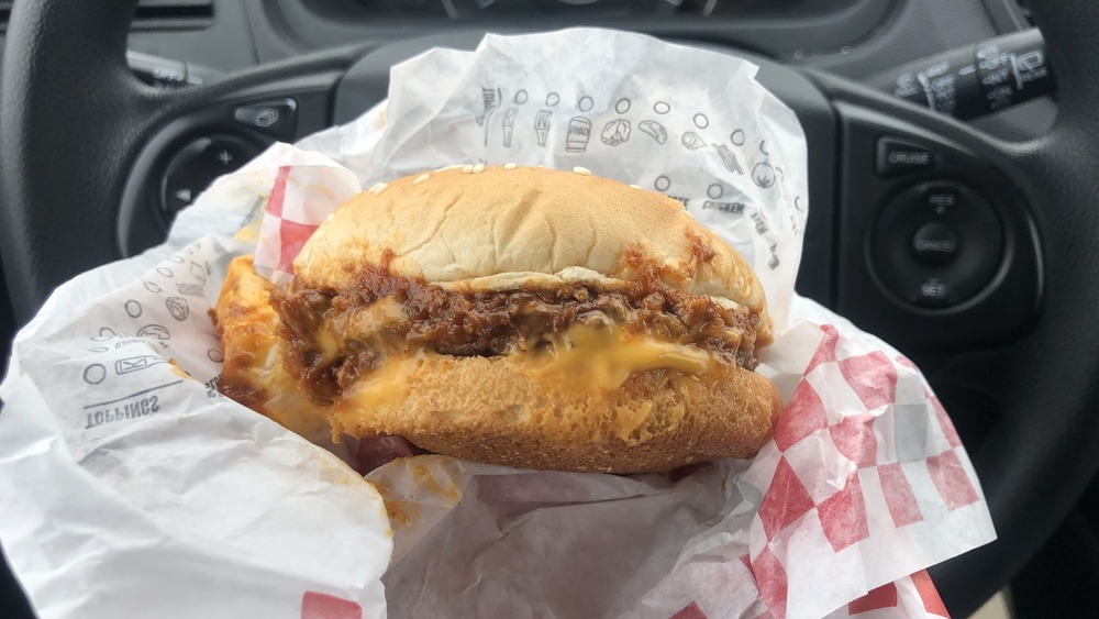 Man holding a Rally's and Checkers hamburger topped with chili 