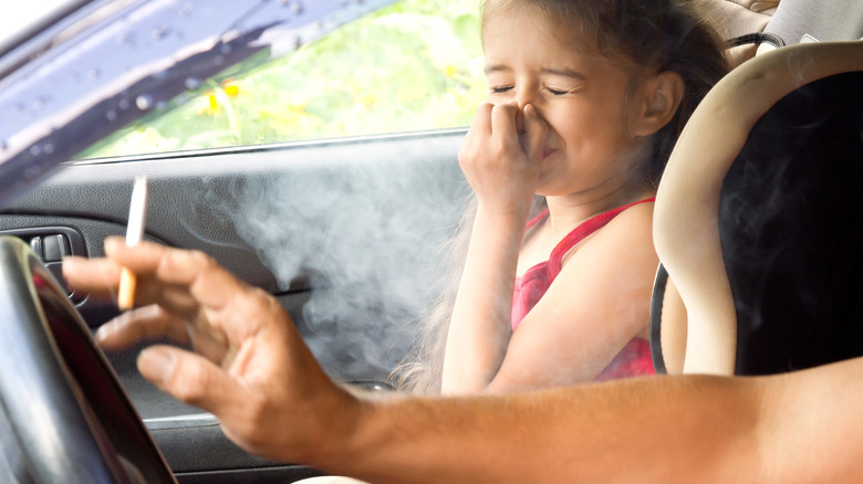 Girl holding nose while parent smokes in car