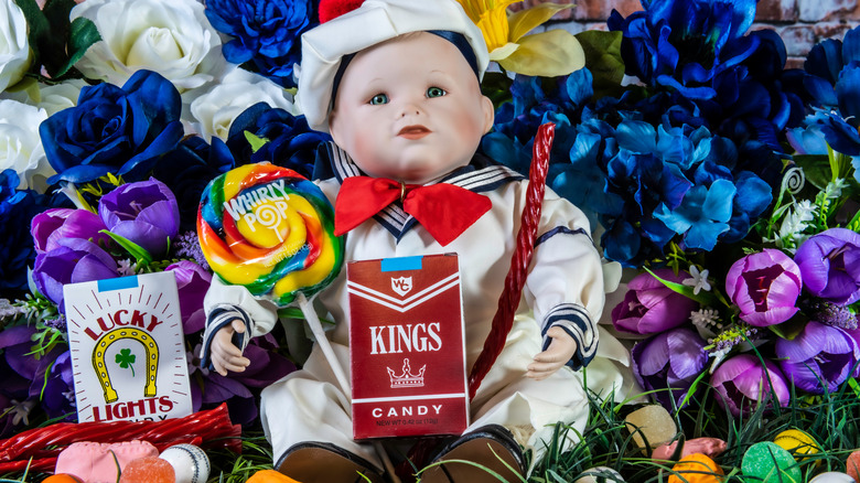 Doll surrounded by candy including cigarette boxes