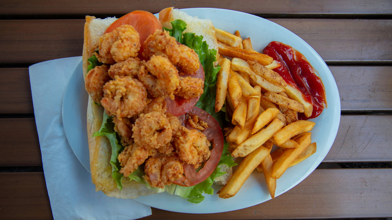 Fried shrimp po' boy on plate with fries and ketchup