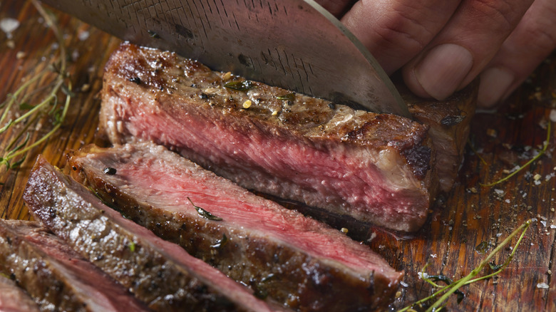 Person slicing a seared and rested steak on a cutting board