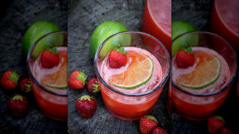 Strawberry lime agua fresca in clear glass next to fresh lime and strawberries