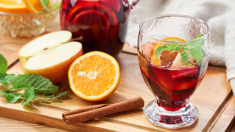 Pitcher and glass of sangria with orange, mint, apple, and cinnamon