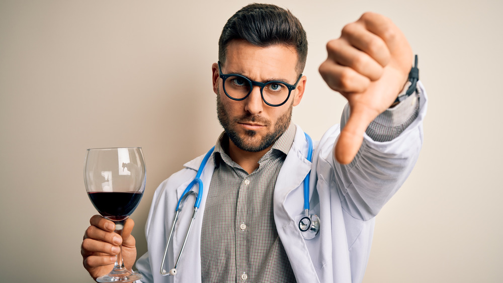 Doctor holding wine glass giving thumbs-down