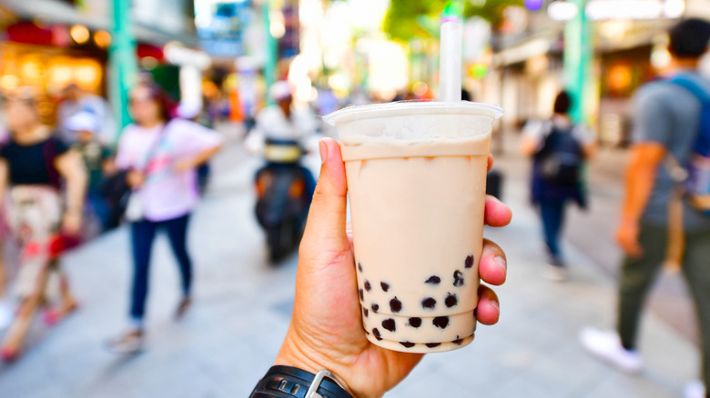 A hand holding a bubble tea on a busy street 