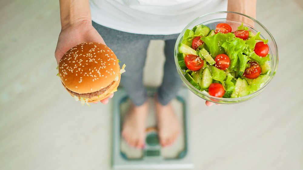 Person on a scale holding a hamburger