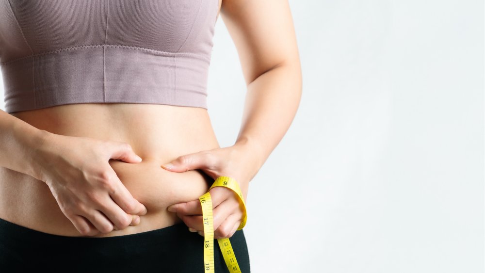 Woman holding belly fat and a tape measure