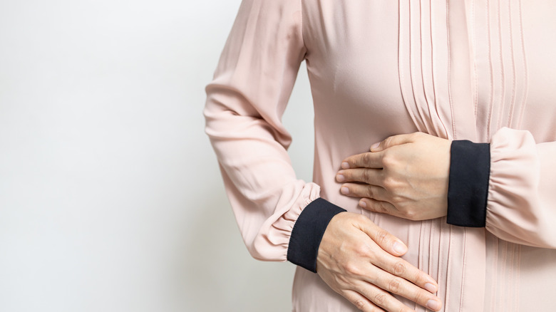 white woman in button-down shirt holding her stomach in pain