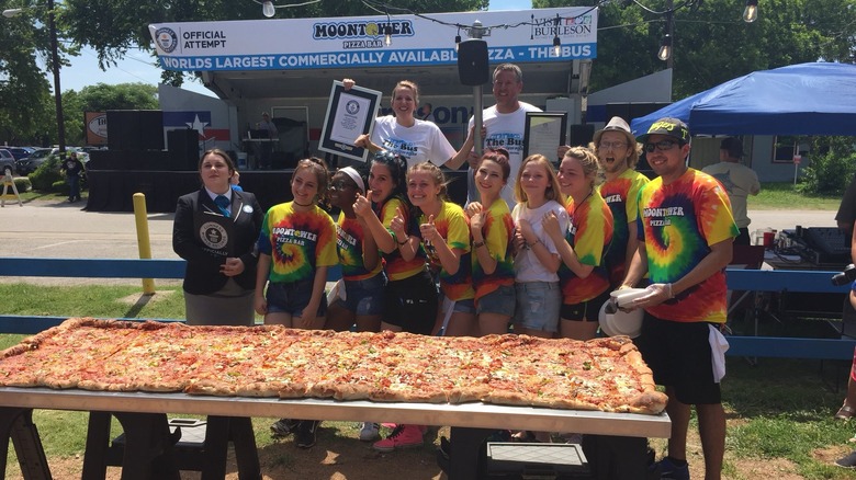 people posing with large pizza