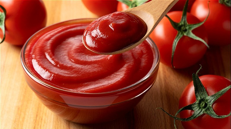 Glass bowl of ketchup with wooden spoon and tomatoes