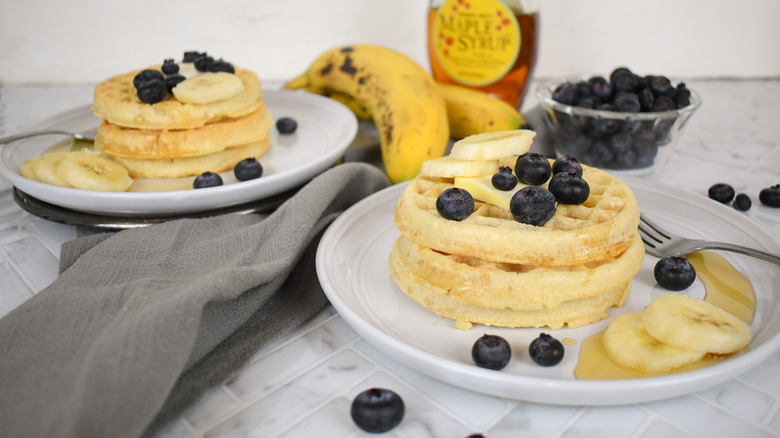 stacks of eggo waffles and ALDI waffles on plates with fruit and maple syrup