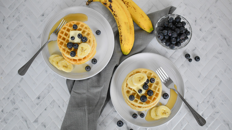 stacks of eggo waffles and ALDI waffles on plates with fruit and maple syrup