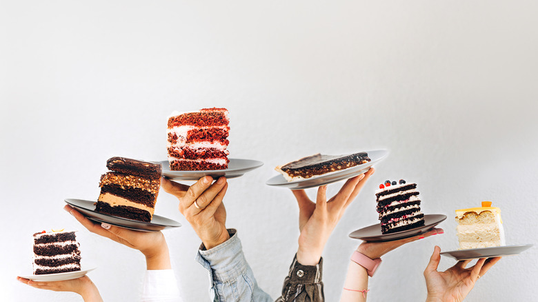 Different hands holding up different cake slices on plates