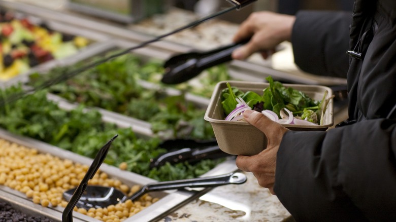 Hands filling a container with salad at a Whole Foods salad bar